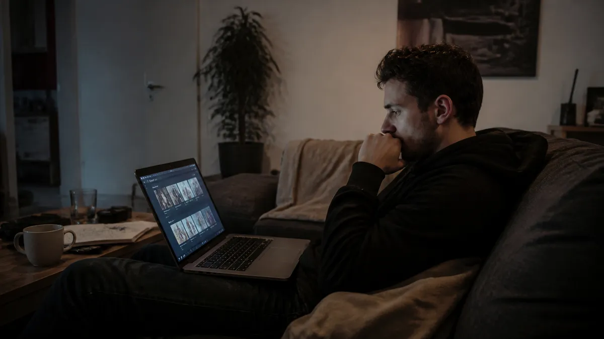 A person sitting on a couch in a dimly lit room, examining drug listings on a laptop.